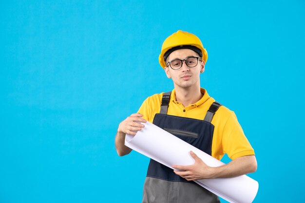 Мужчина-строитель в униформе с бумажным планом на синем, вид спереди
