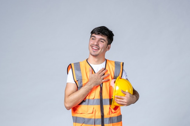 front view of male builder in uniform with protective helmet on white wall