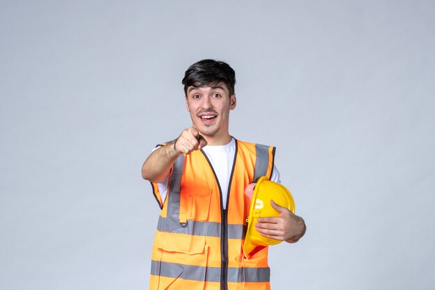front view of male builder in uniform with protective helmet on white wall