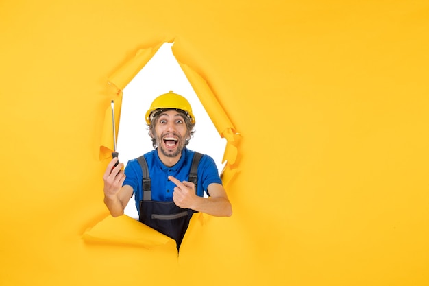 Вид спереди мужчина-строитель в униформе с отверткой на желтой стене строительный рабочий-строитель цветная работа