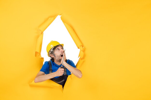 Вид спереди мужчина-строитель в униформе с отверткой на желтой стене работает конструктор, здание цветной рабочий архитектурная работа