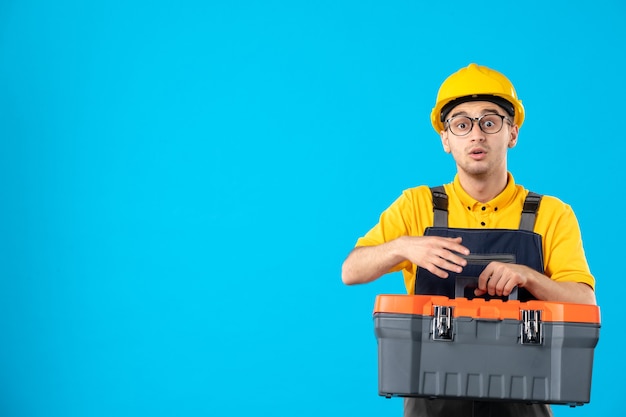 Vista frontale del costruttore maschio in uniforme con cassetta degli attrezzi nelle sue mani sulla parete blu