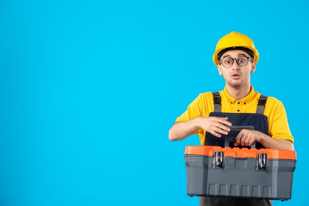 Вид спереди мужчины-строителя в униформе с ящиком для инструментов в руках на синей стене