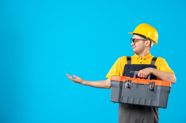 Front view of male builder in uniform with tool box in his hands on blue wall