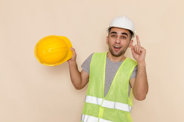 Front view male builder in white helmet holding yellow helmet on the cream background