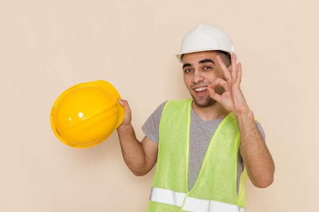 Costruttore maschio di vista frontale in casco bianco che tiene casco giallo sui precedenti chiari