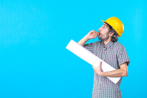 青い背景のエンジニア労働者コンストラクタージョブプロパティアーキテクチャの建物に彼の手で計画を持つ正面図の男性ビルダー
