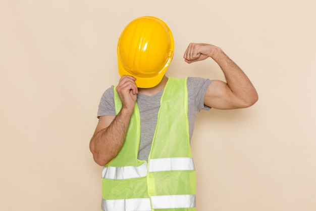 Free photo front view male builder in yellow helmet hiding his face flexing on light desk