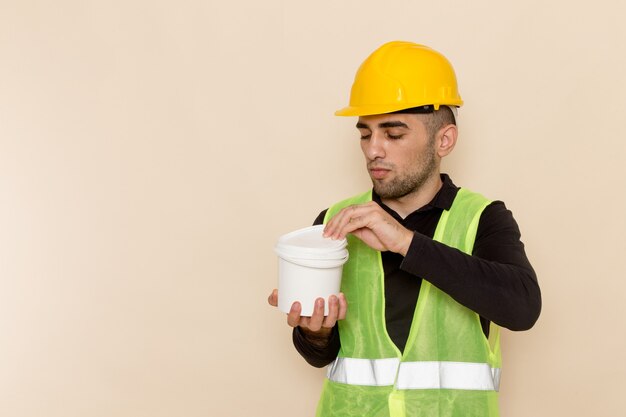 Front view male builder in yellow helmet holding paint on light background