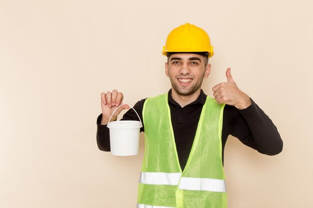 Front view male builder in yellow helmet holding paint on light background
