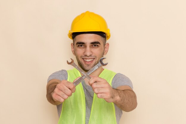 Вид спереди мужчина-строитель в желтом шлеме, держащий серебряный инструмент и улыбающийся на светлом фоне