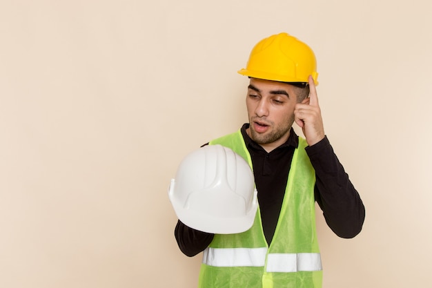 Front view male builder in yellow helmet holding white helmet on light background