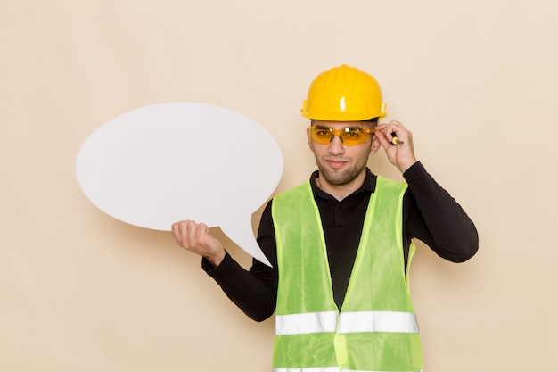 Вид спереди мужчина-строитель в желтом шлеме с белым знаком на светлом столе