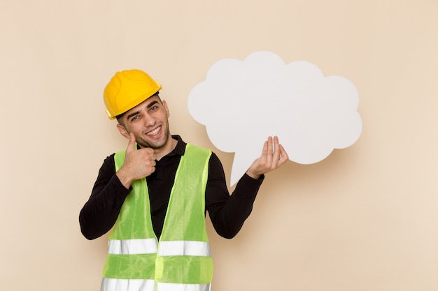 Free photo front view male builder in yellow helmet holding white sign and smiling on light background