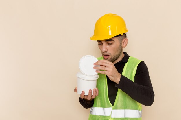 Front view male builder in yellow helmet opening paint on light desk