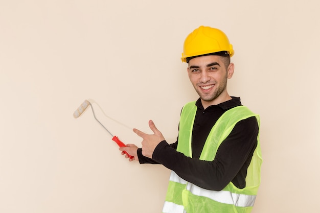 Front view male builder in yellow helmet painting walls on light background