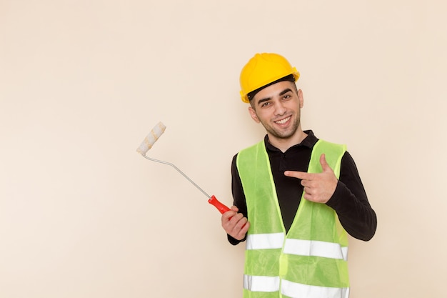 Front view male builder in yellow helmet painting walls on the light background