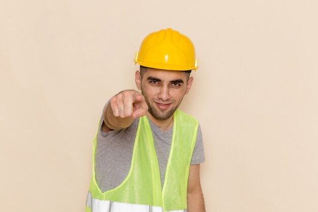 Вид спереди мужчина-строитель в желтом шлеме, указывая на светлом фоне