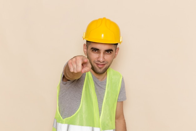 Front view male builder in yellow helmet pointing out on light background