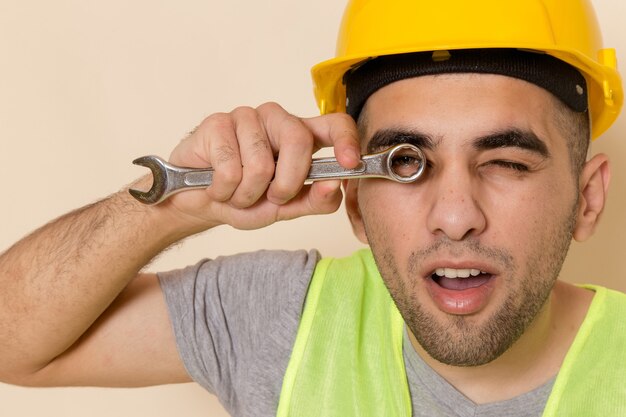 Front view male builder in yellow helmet posing holding tool on light background