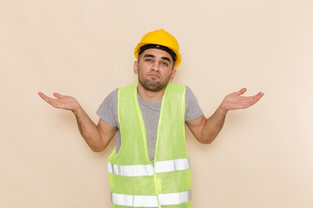 Front view male builder in yellow helmet posing on the light background