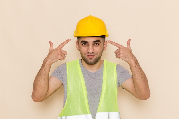 Front view male builder in yellow helmet posing with delighted expression on light background