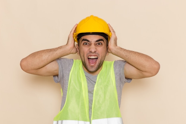Front view male builder in yellow helmet posing with excited expression on the light background