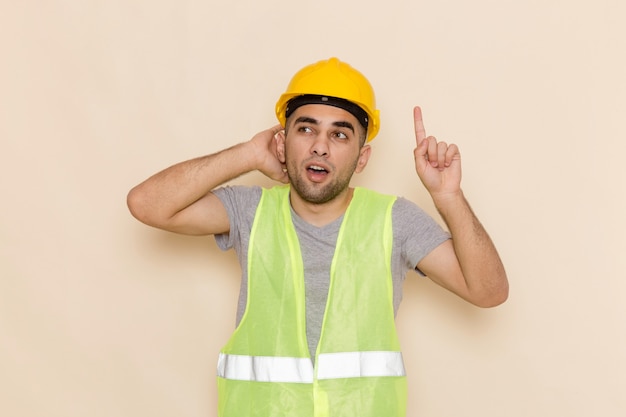 Front view male builder in yellow helmet posing with raised finger on light background