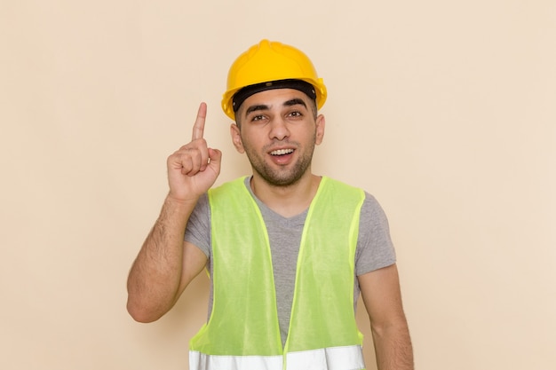 Front view male builder in yellow helmet posing with raised finger on the light background