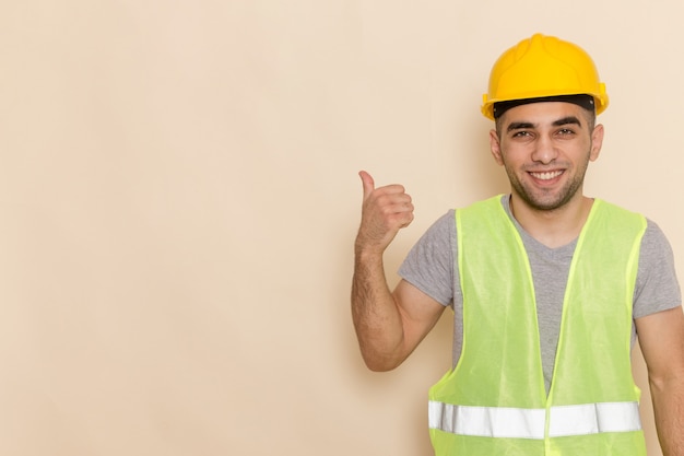 Вид спереди мужчина-строитель в желтом шлеме позирует с улыбкой на светлом фоне
