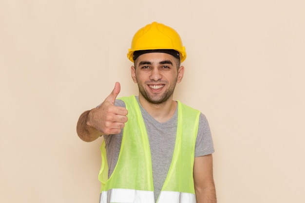 Front view male builder in yellow helmet smiling and posing on cream background