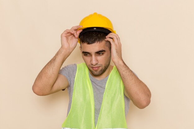 Front view male builder in yellow helmet taking it off on light desk