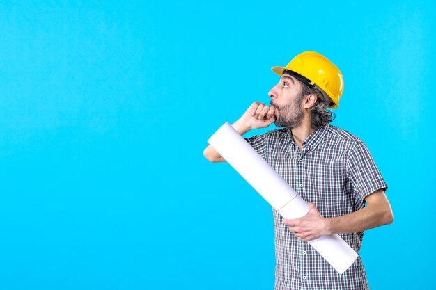 Front view male builder in yellow helmet with plan on blue background building architecture constructor color property worker job engineer