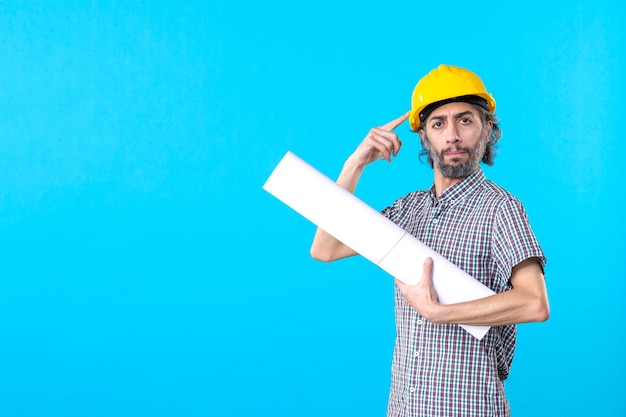 Вид спереди мужчина-строитель в желтом шлеме с планом на синем фоне, архитектура здания, строитель, инженер-строитель