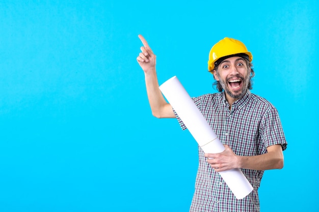 Вид спереди мужской строитель в желтом шлеме с планом на синем фоне строительный рабочий архитектура конструктор цвет плоская собственность