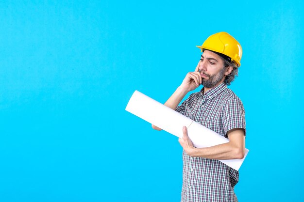 Front view male builder in yellow helmet with plan on a blue background property architecture constructor worker building job engineer