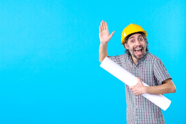 Front view male builder in yellow helmet with plan on blue background worker property architecture constructor building job engineers