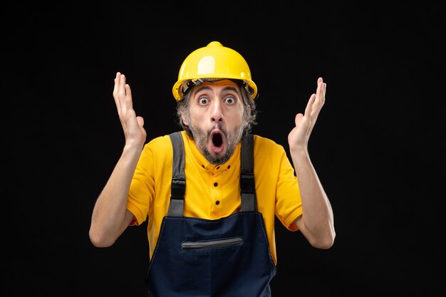 Front view of male builder in yellow uniform on a black wall