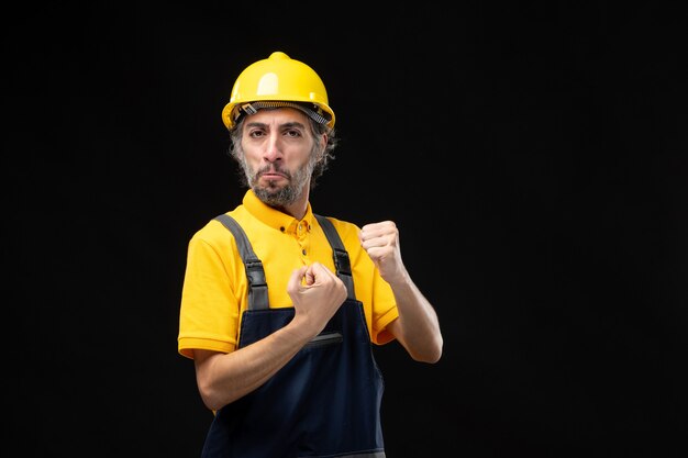 Front view of male builder in yellow uniform on black wall