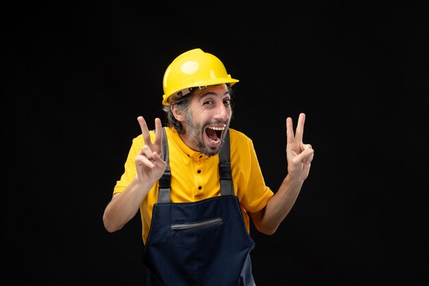 Vista frontale del costruttore maschio in uniforme gialla sul muro nero