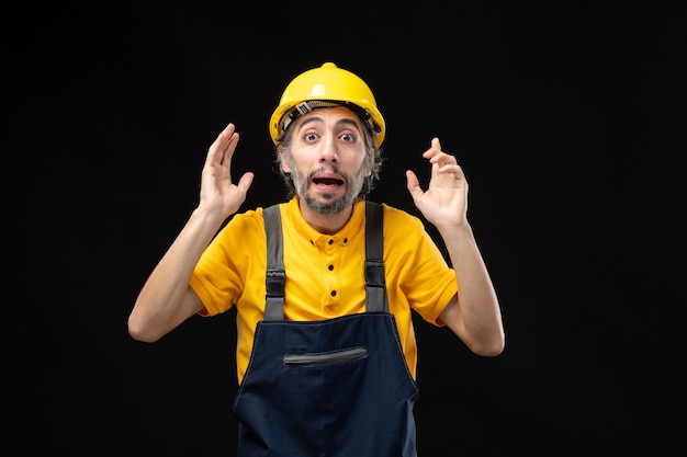 Front view of male builder in yellow uniform on black wall