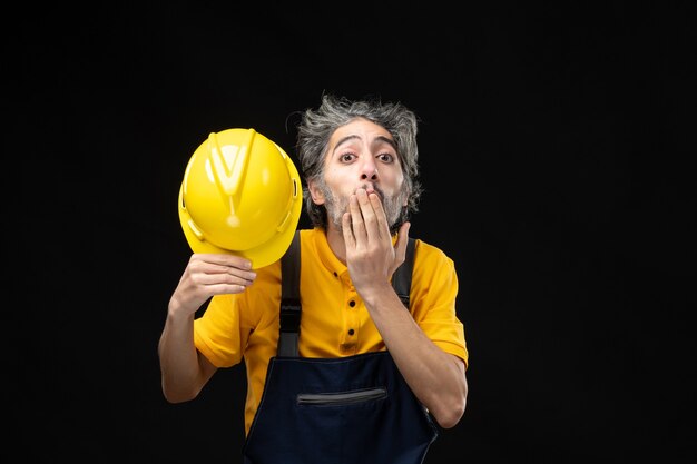 Front view of male builder in yellow uniform on black wall