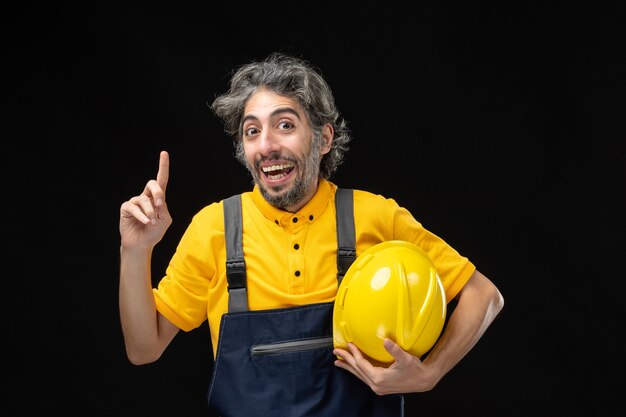 Front view of male builder in yellow uniform on black wall