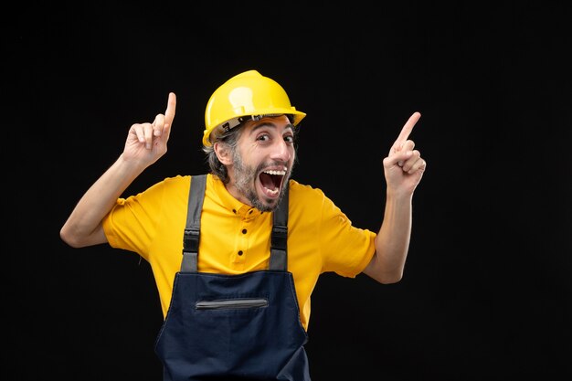 Вид спереди мужчины-строителя в желтой форме на черной стене