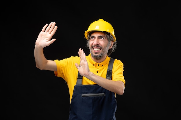 Front view of male builder in yellow uniform on the black wall