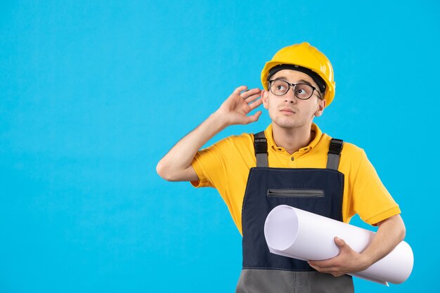 Вид спереди мужчина-строитель в желтой форме с бумажным планом на синем