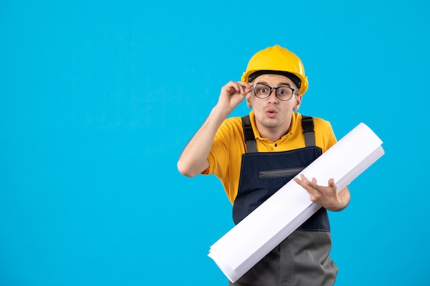 Front view male builder in yellow uniform with paper plan on blue 