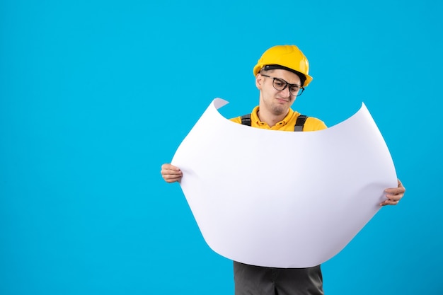 Front view of male builder in yellow uniform with plan on blue 