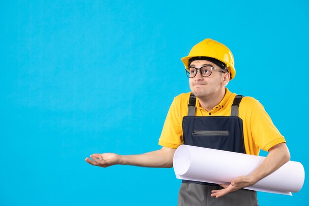 Front view of male builder in yellow uniform with plan on blue 