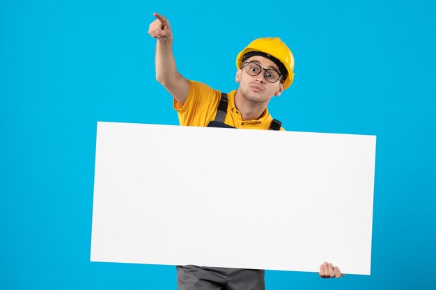 Front view of male builder in yellow uniform with plan on blue 